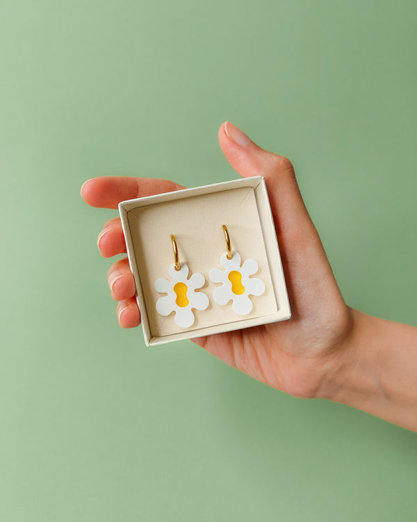 Hand hält Schmuckbox mit weiß gelben Blumen Ohrringen aus Acryl an goldenen Creolen