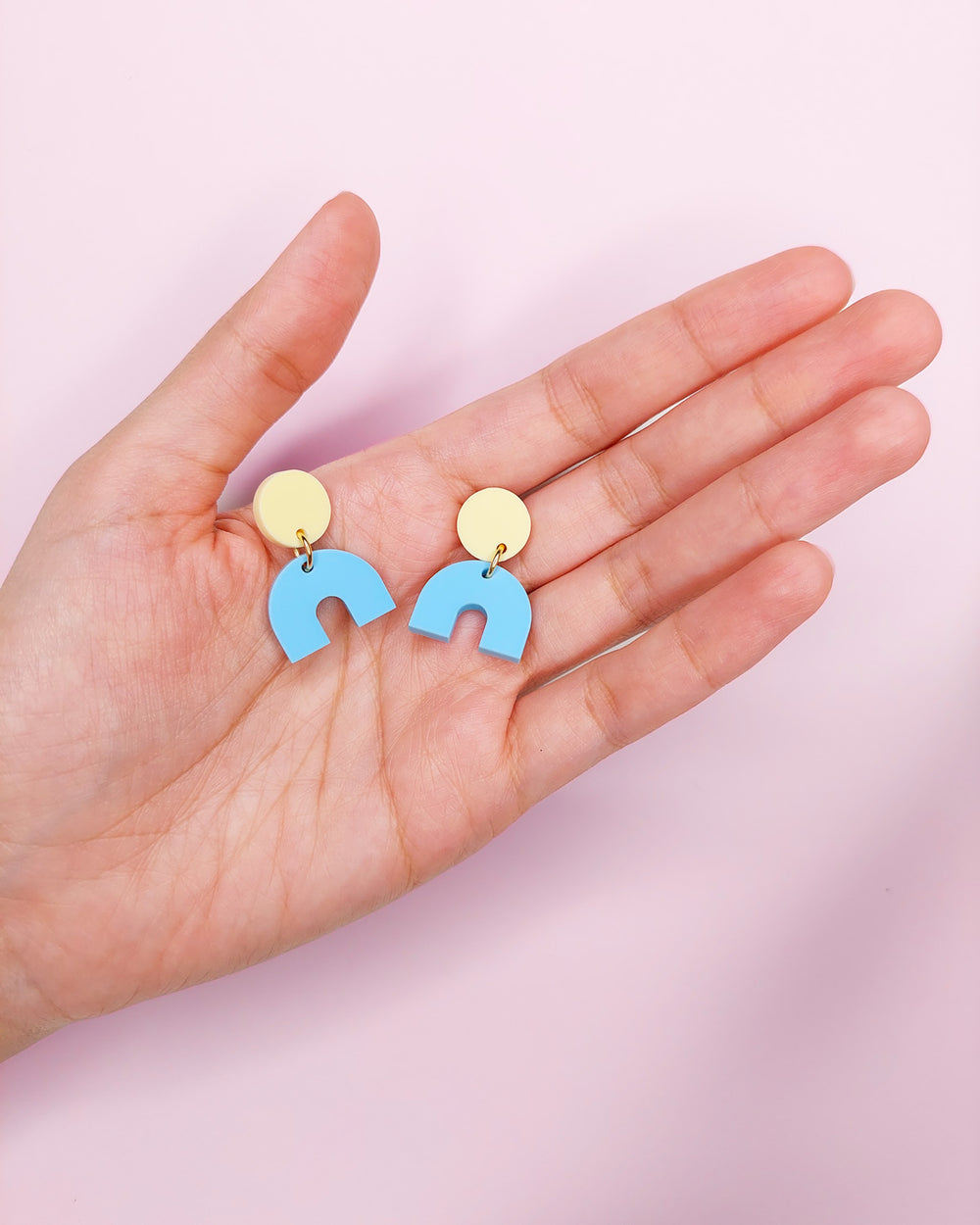 Hand mit bunten pastell Bogen Ohrringen aus Acryl 